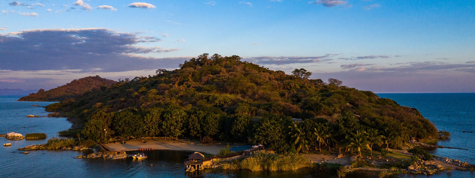 Photo of a small, private island with a lodge, palm trees, and a beach on Lake Malawi.